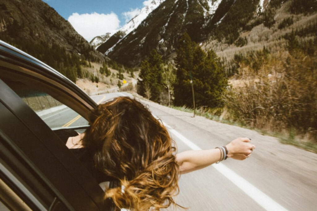 A woman riding in the passenger seat of a car with her arms outstretched on the road.