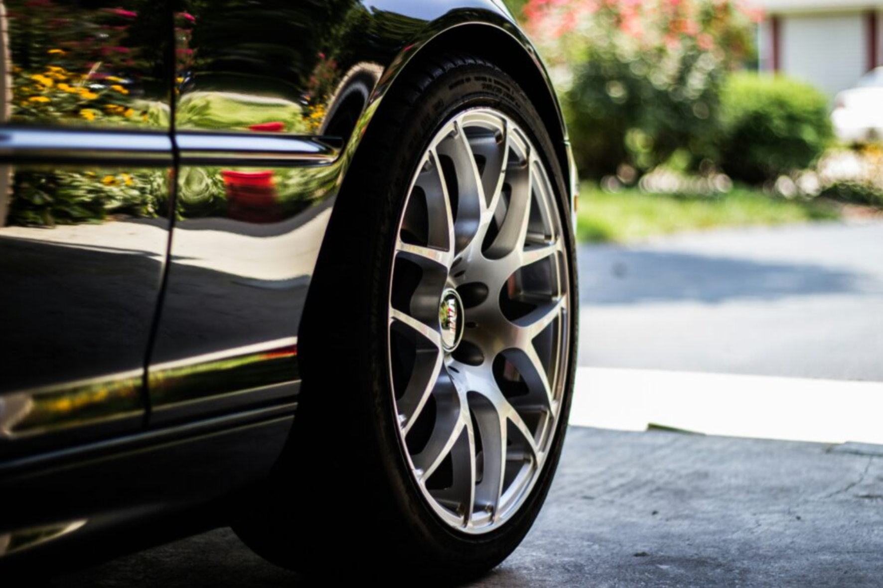 A close up of a black car with a tire and shiny rims.