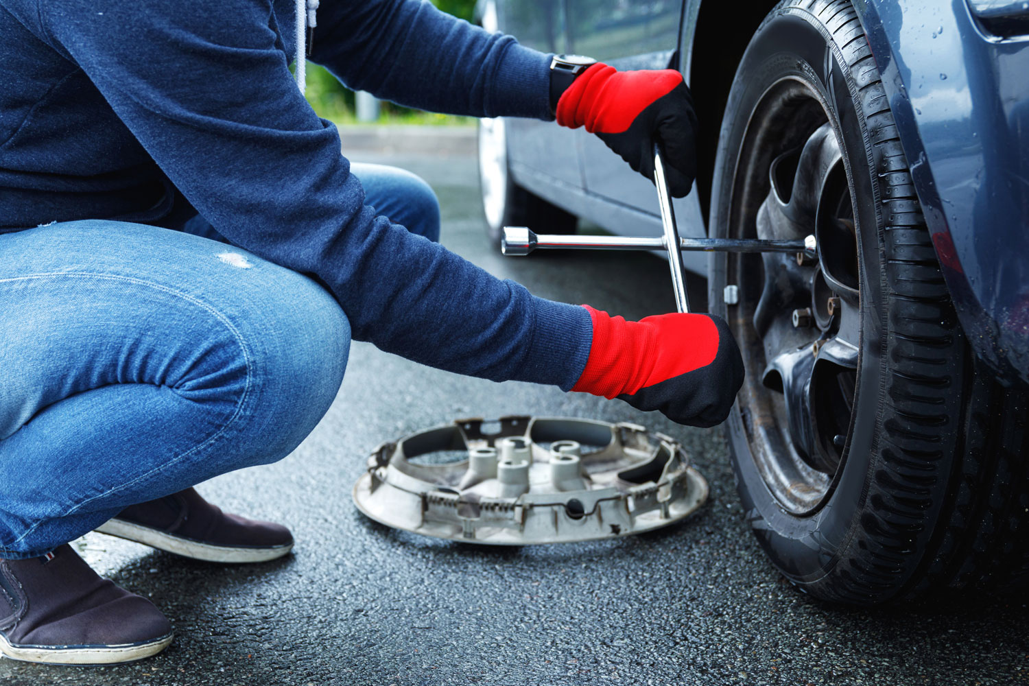 A driver using a tire repair kit on a damaged tire for a temporary fix.