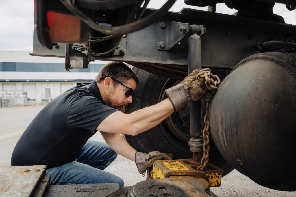 Tow Pro technician securing heavy-duty towing equipment on a truck axle during long distance haul preparation.