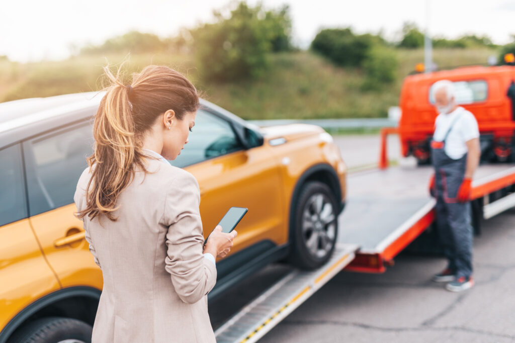 Tow truck lifting a car during an impound process in a no parking zone, with the car owner standing nearby using her phone to navigate the situation.