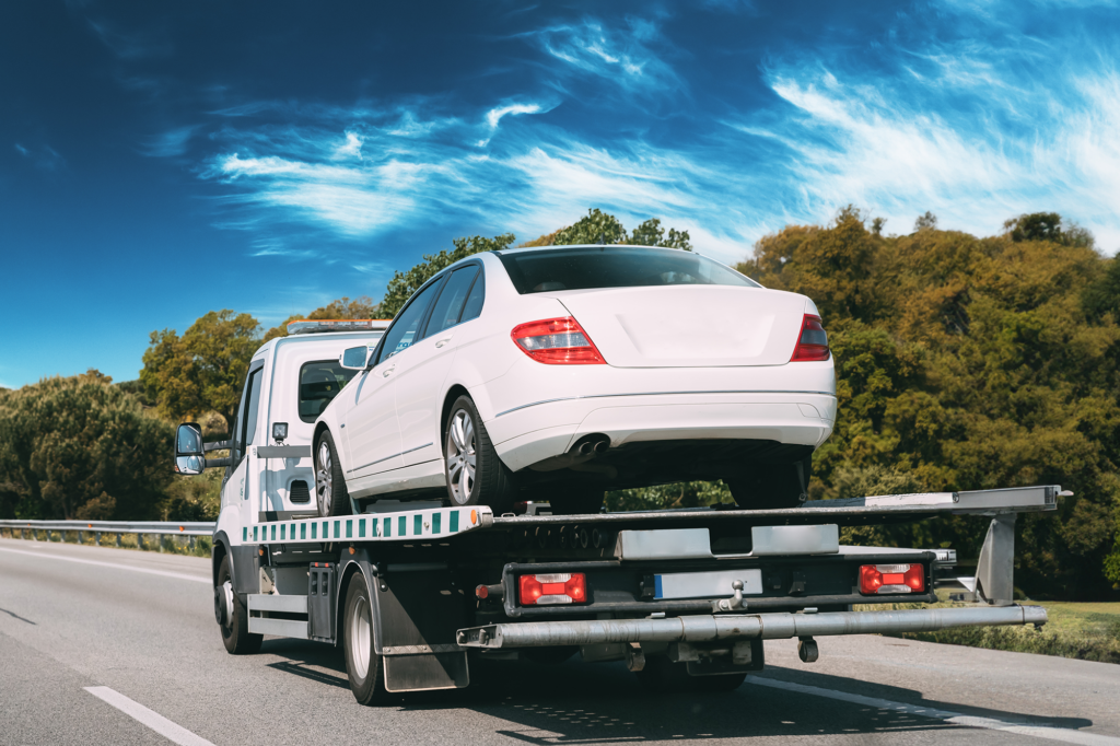 Flatbed tow truck loading a vehicle on the side of the highway.