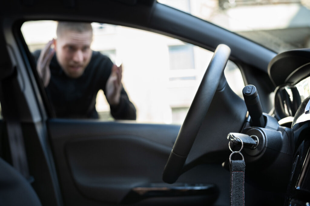 Frustrated man standing outside his locked car, looking in at keys left inside on the ignition capturing a common car lockout situation and the urgent need for roadside assistance.