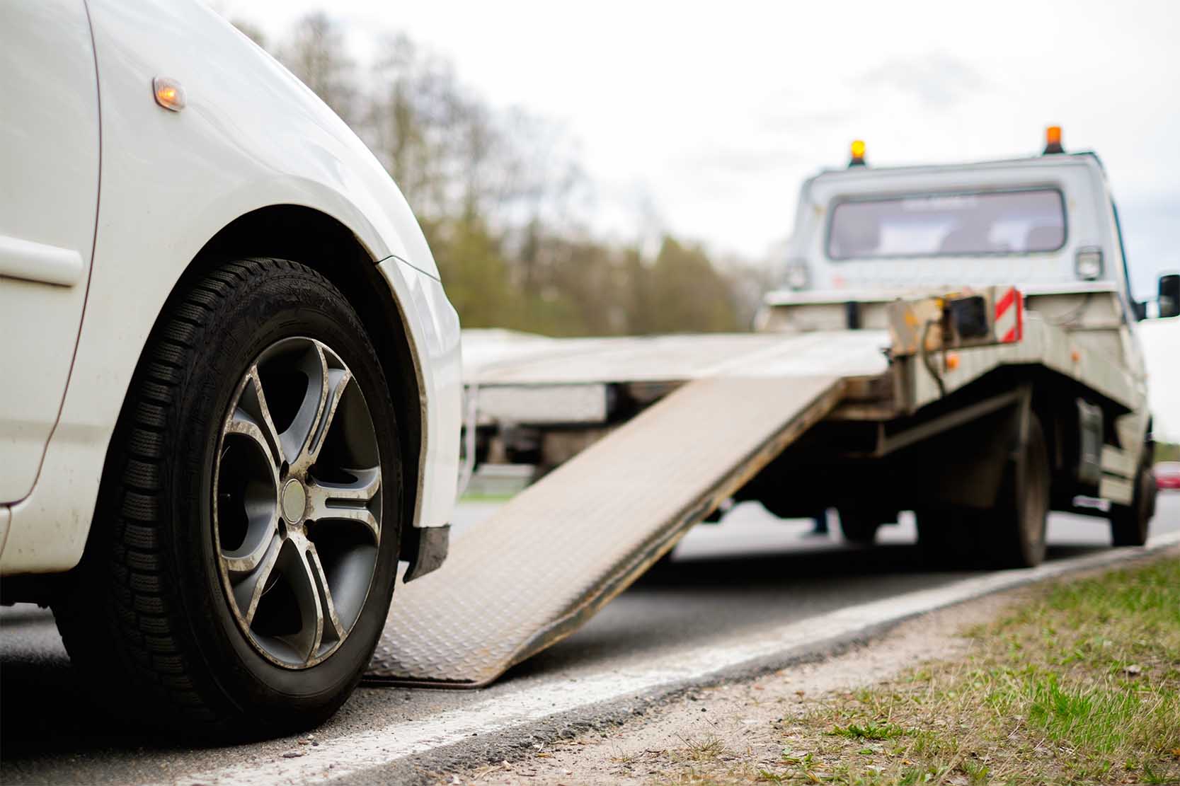 A white vehicle getting loaded onto a tow truck on the roadside.