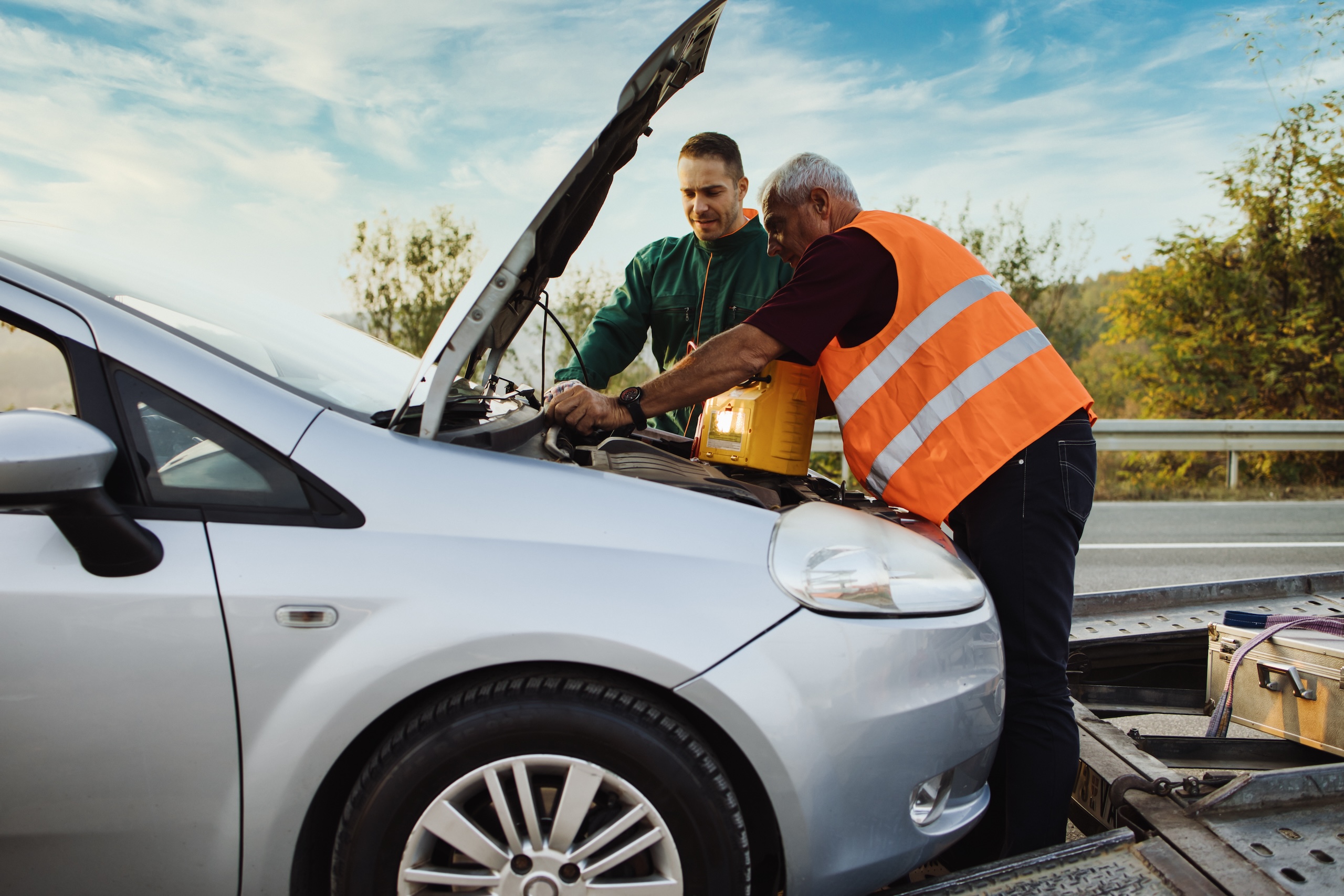 Roadside assistance technician jump-starting a vehicle after a dead battery, showing how long does a car battery last before failure.
