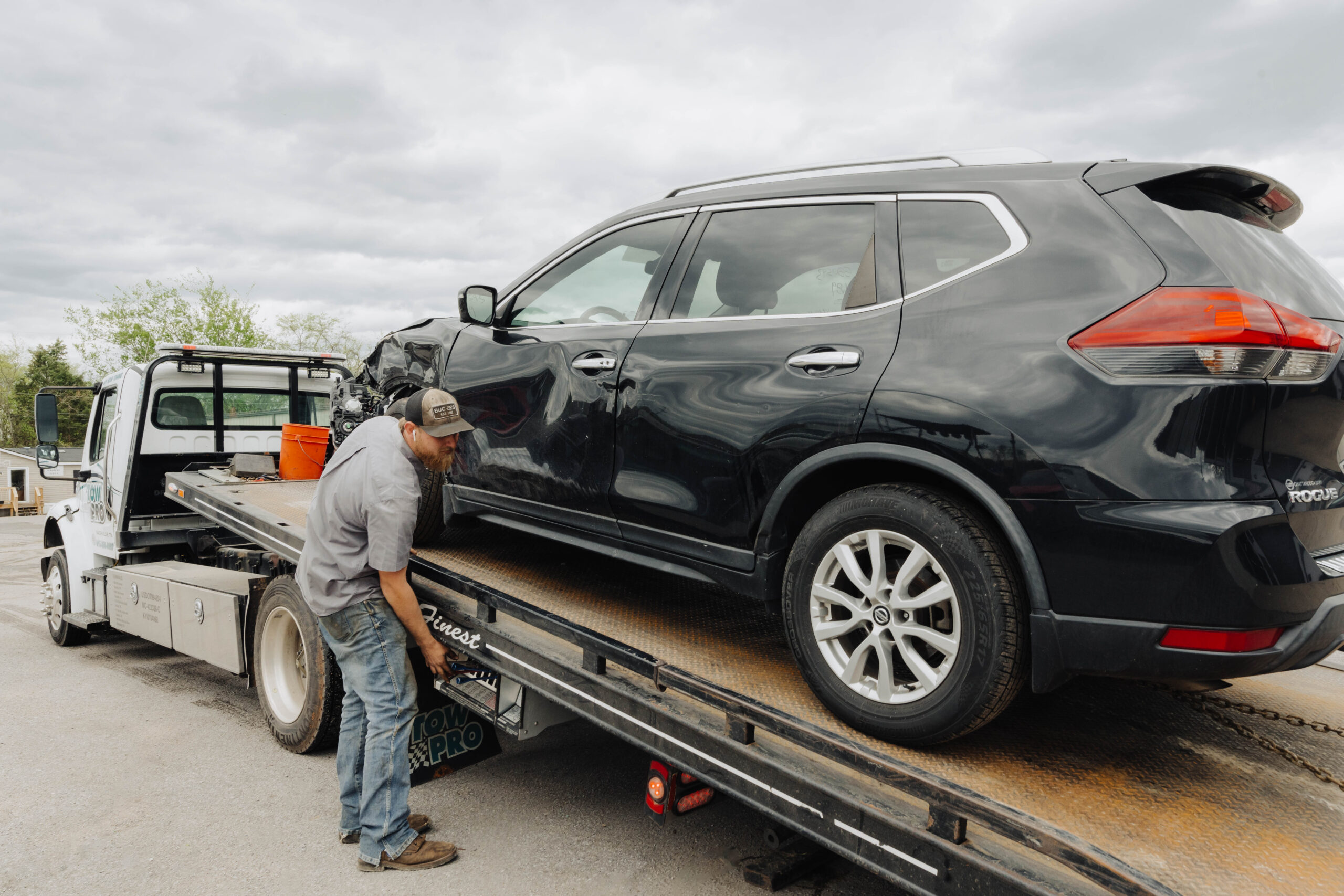 A Tow Pro technician loading a damaged black SUV onto a flatbed tow truck in Tennessee after a car accident. 