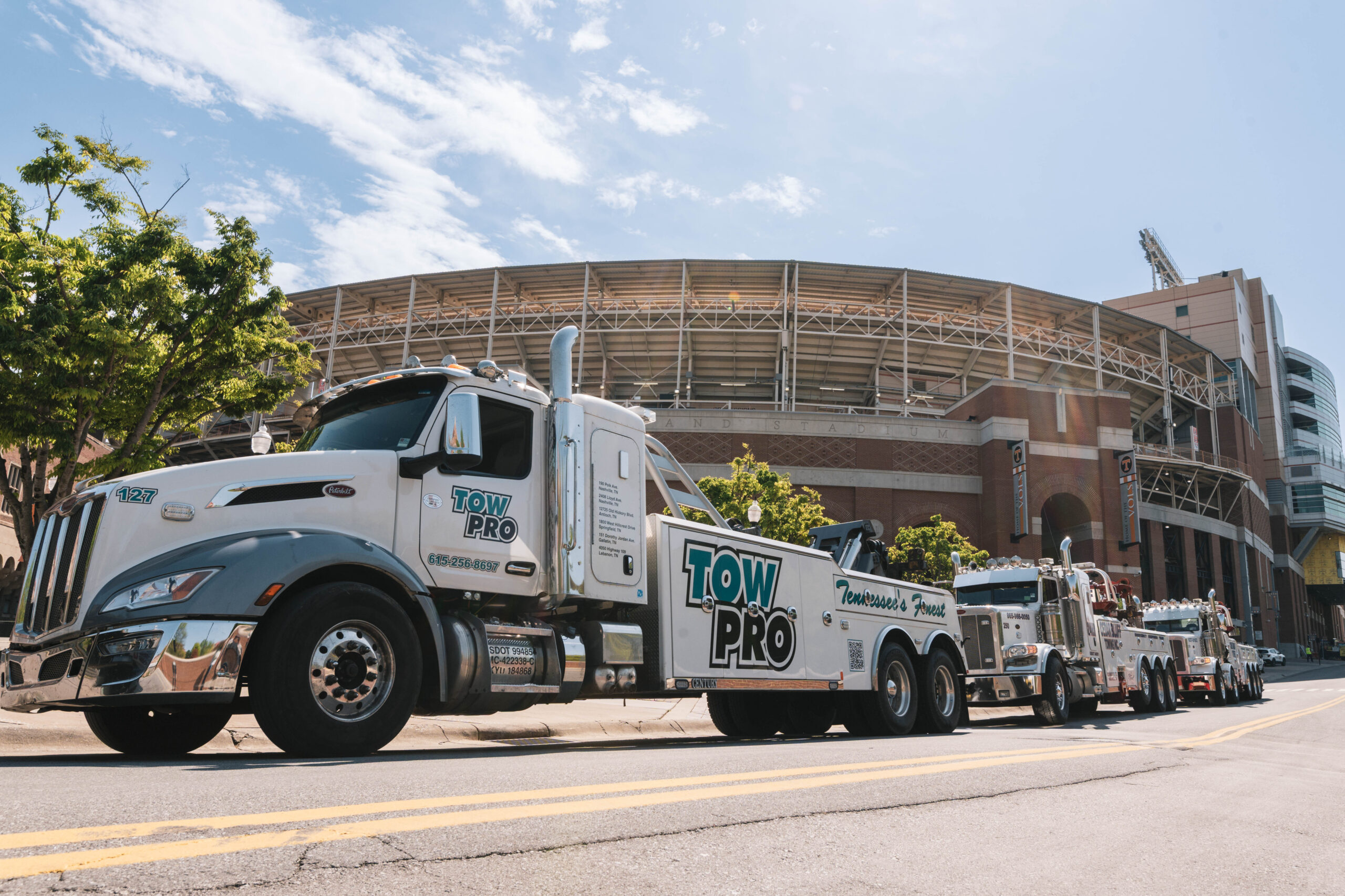 A line of professional Tow Pro heavy-duty tow trucks parked in front of Neyland Stadium, showcasing the reliable fleet available for Nashville junk car removal and recovery services.
