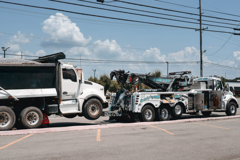 A Tow Pro heavy-duty wrecker truck successfully lifting and towing a large dump truck, demonstrating expert wrecker truck driver services in Middle Tennessee.